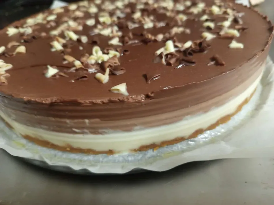Pastel de chocolate con capas de ganache brillante y crema blanca, cubierto con nueces picadas en un plato.