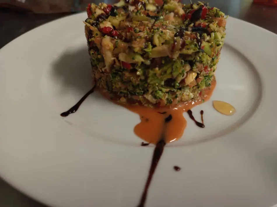 Tarta colorida de verduras cortadas en dados sobre un plato blanco con un chorrito de salsa balsámica.