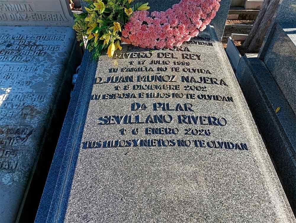 Lápida con una inscripción. Coronada con una corona rosa y flores amarillas.