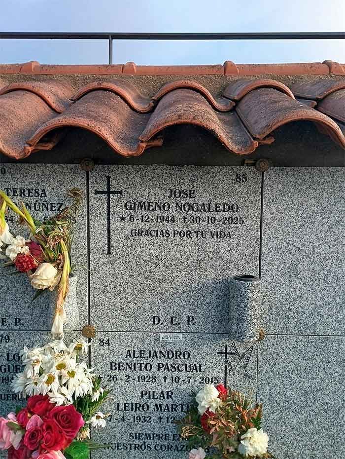 Lápidas con nombres, fechas y arreglos florales bajo un techo de tejas.