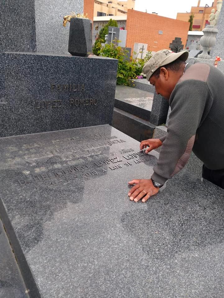 Hombre junto a una tumba, tocando la lápida con inscripciones. Cementerio con lápida de granito oscuro.