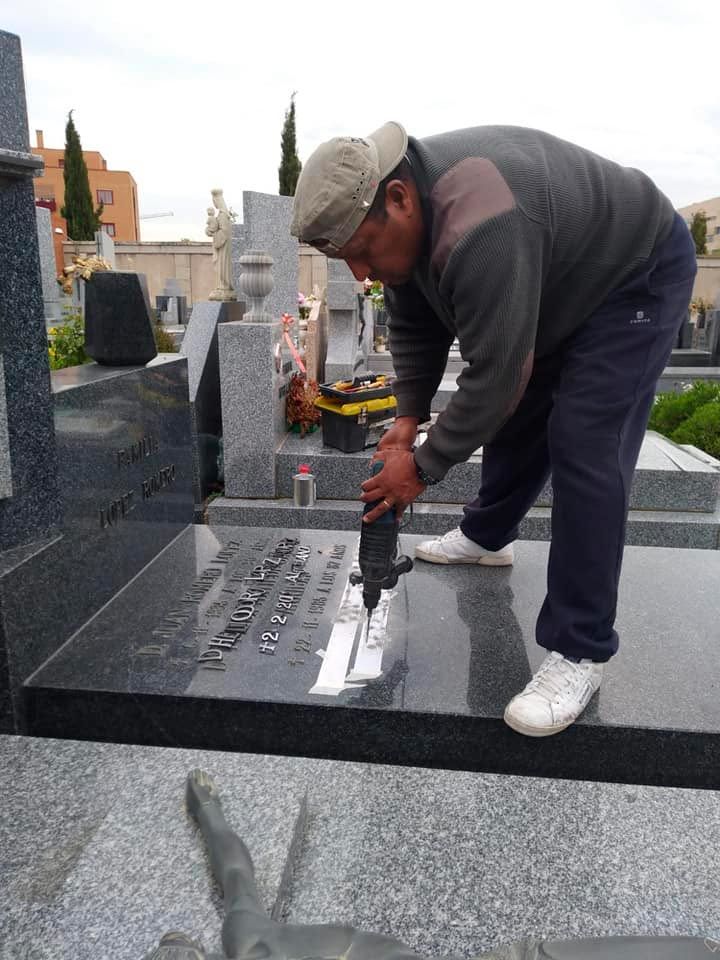 Hombre usando un taladro en una lápida en un cementerio.