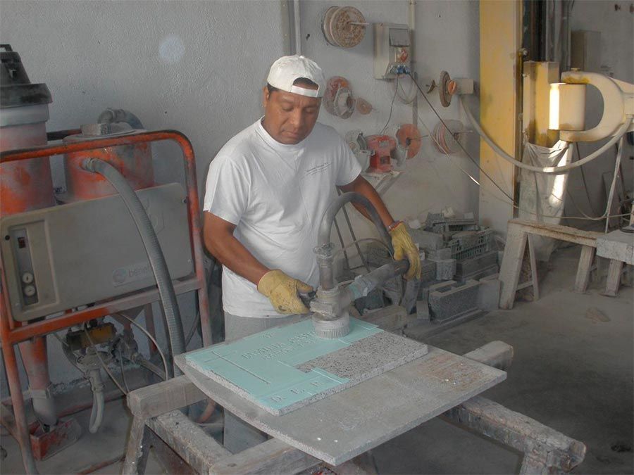 Hombre que utiliza una lijadora eléctrica sobre una baldosa de piedra en un taller, con guantes y gorra.