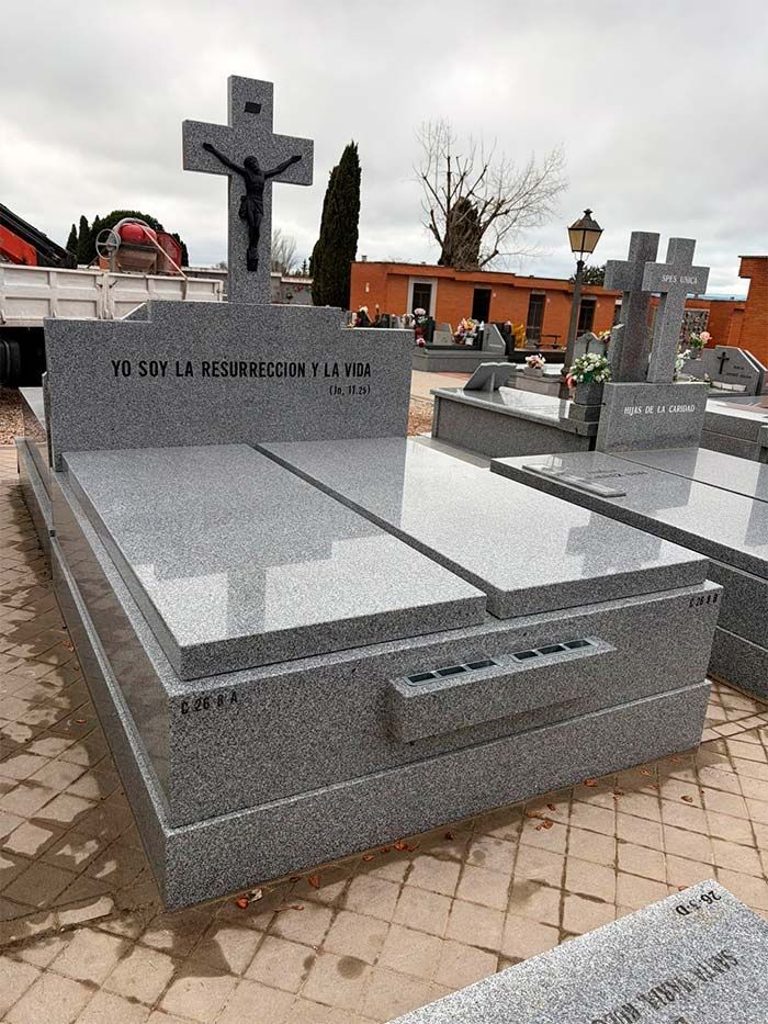 Lápida de granito gris con cruz y epitafio en un cementerio.