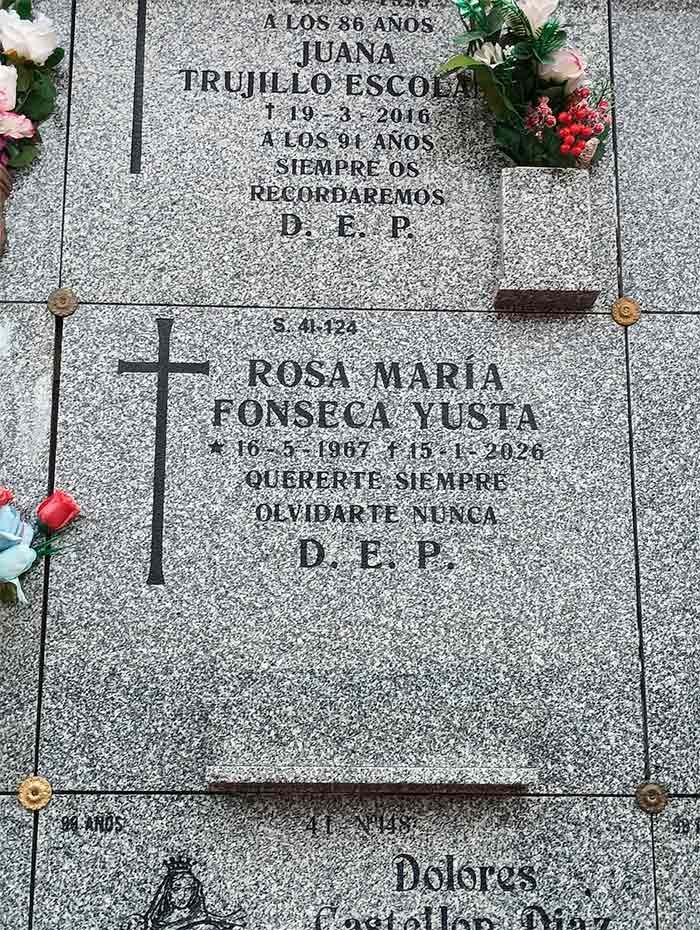 Lápida con inscripciones, cruz y flores. 