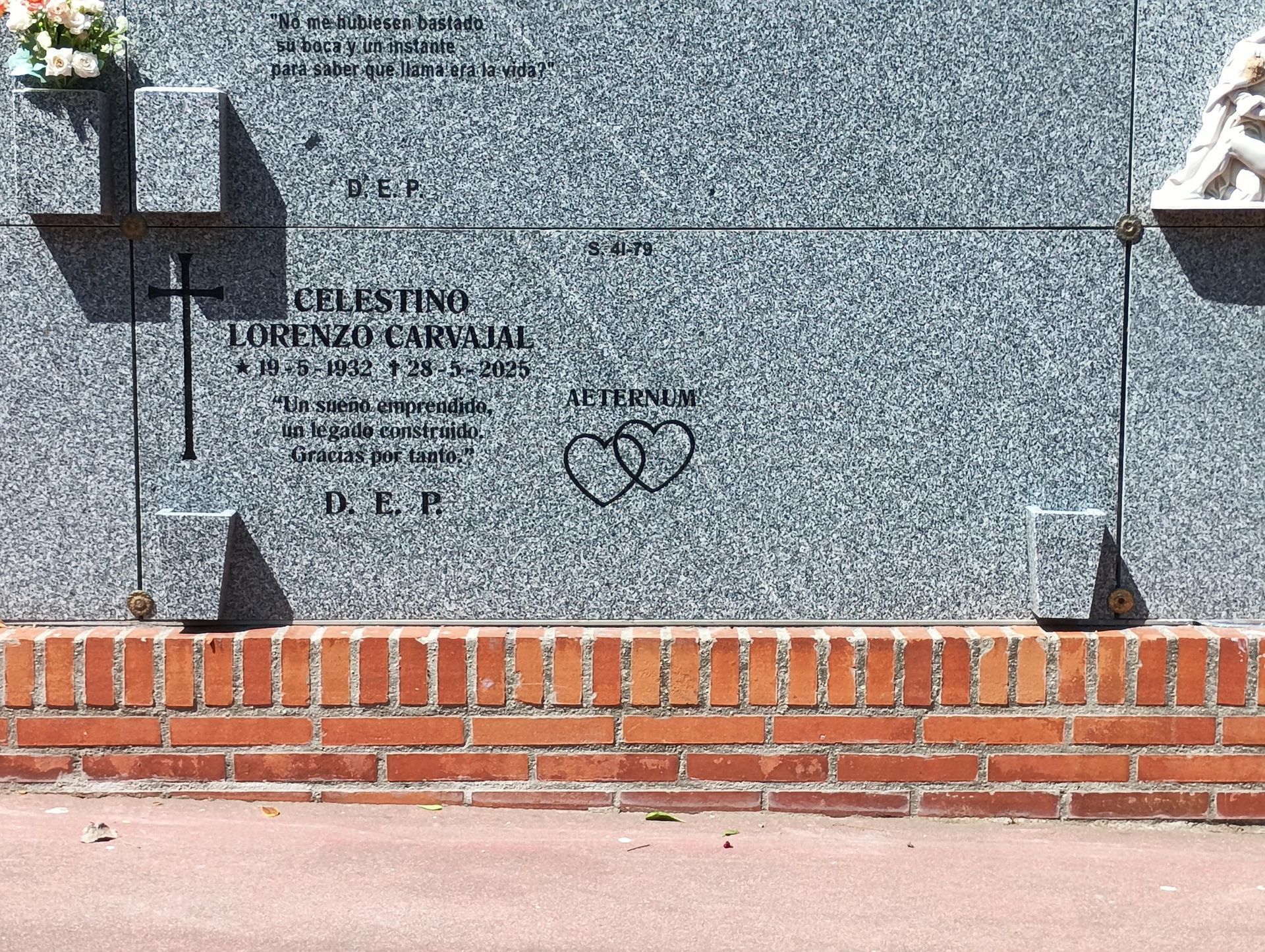 Lápida con inscripción, cruz y dos corazones unidos. Piedra de granito sobre base de ladrillo.