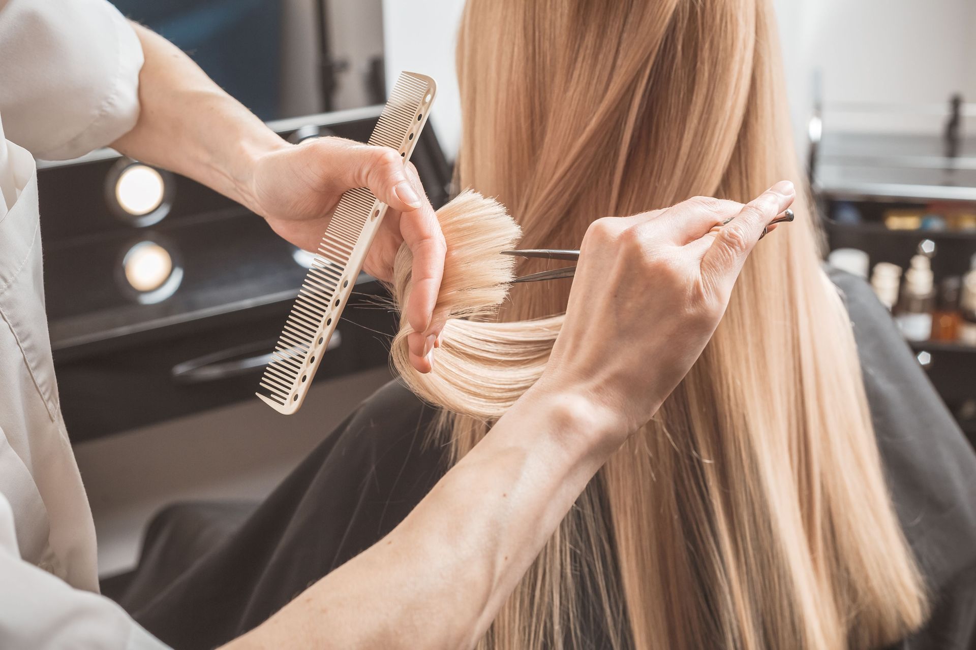 Un coiffeur démêle de longs cheveux blonds dans un salon tout en tenant des ciseaux et une brosse ronde
