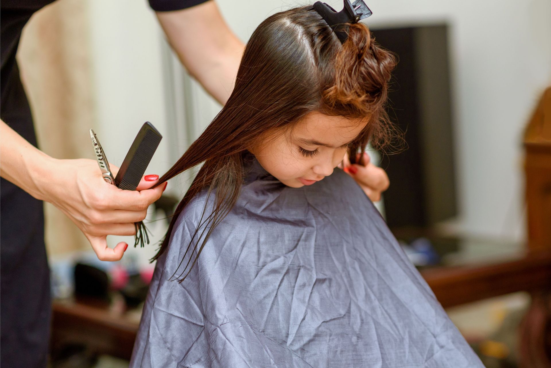 Enfant se faisant couper les cheveux, assis sous une cape de coiffure grise