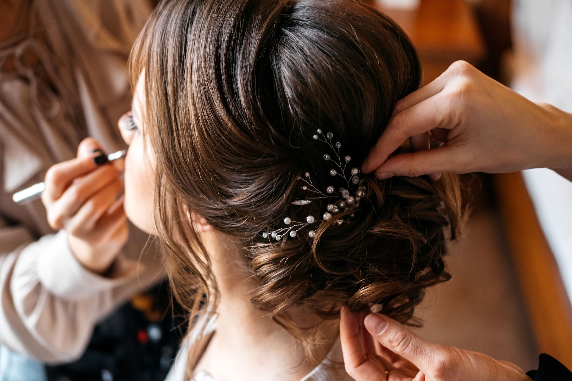 Une coiffeuse fixe un accessoire floral dans un chignon élégant pendant qu’une autre personne coiffe les cheveux