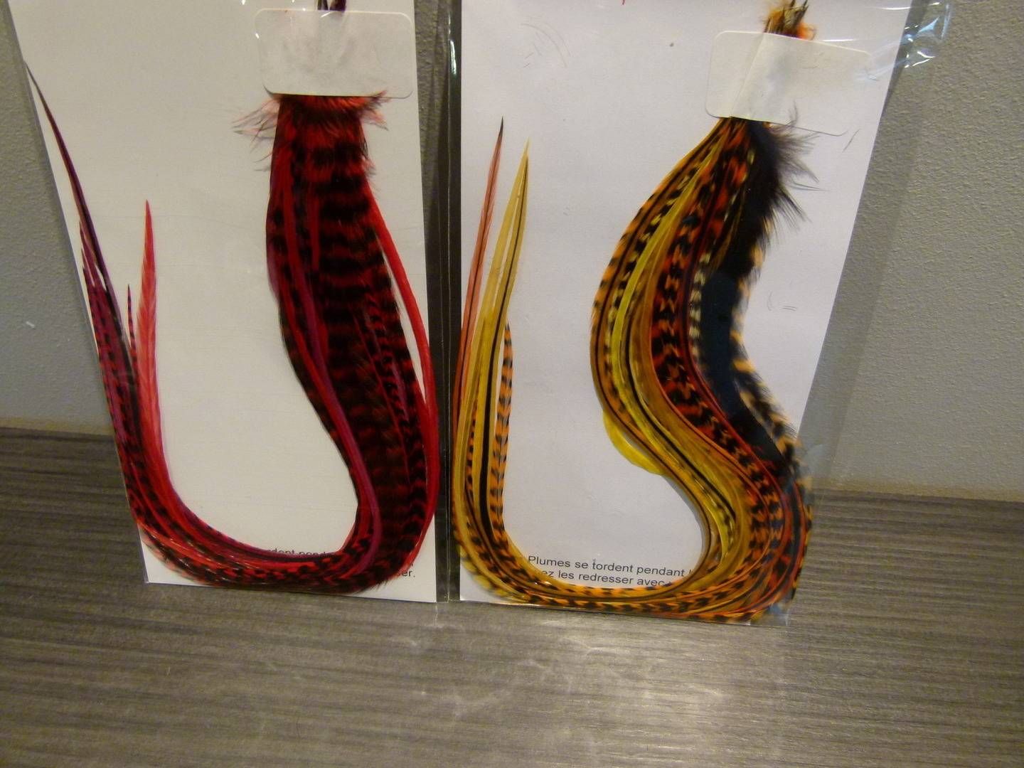 Deux mouches leurres colorées à plumes, avec des queues incurvées, présentées côte à côte sur des cartes blanches