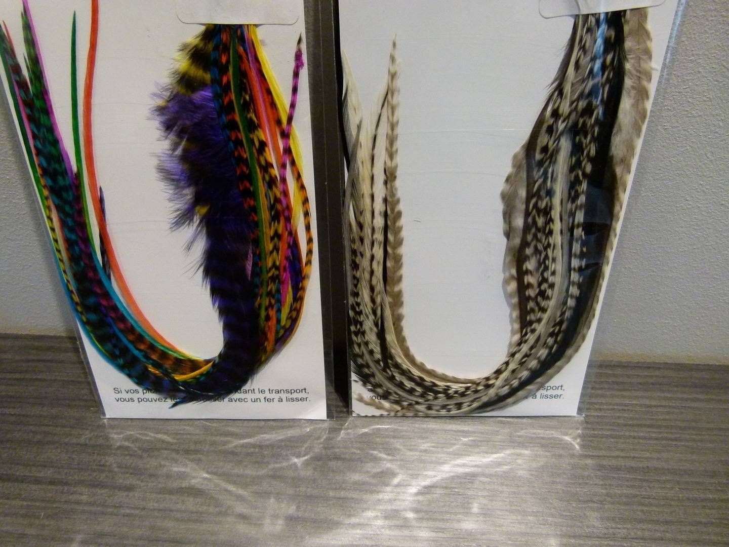 Deux extensions de cheveux décoratifs à plumes présentés sur des supports blancs, l’un multicolore et l’autre noir et or
