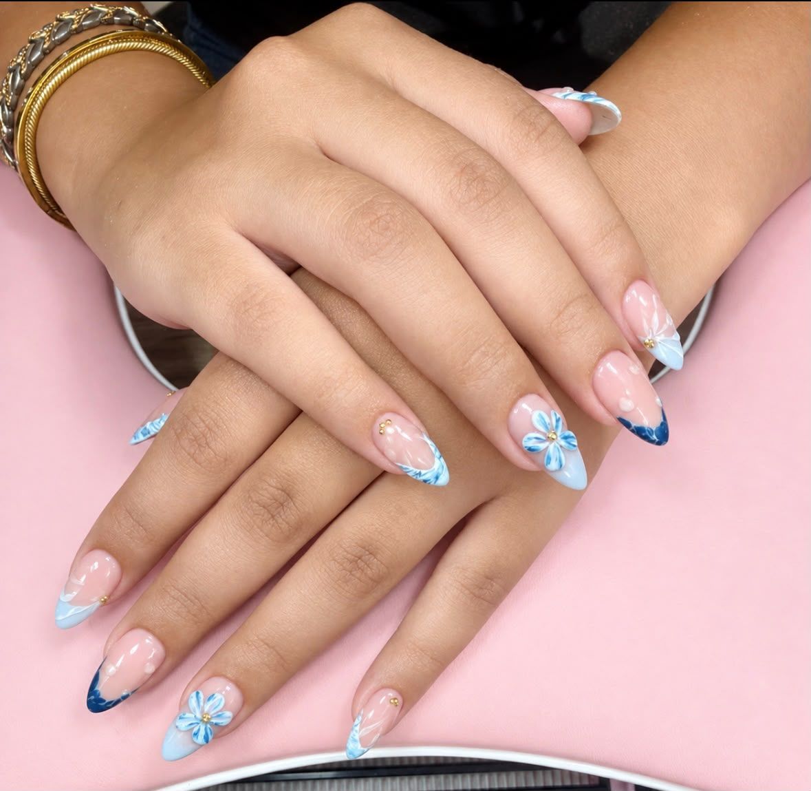 Manos con uñas largas de color azul pastel con estampado floral sobre un fondo rosa.