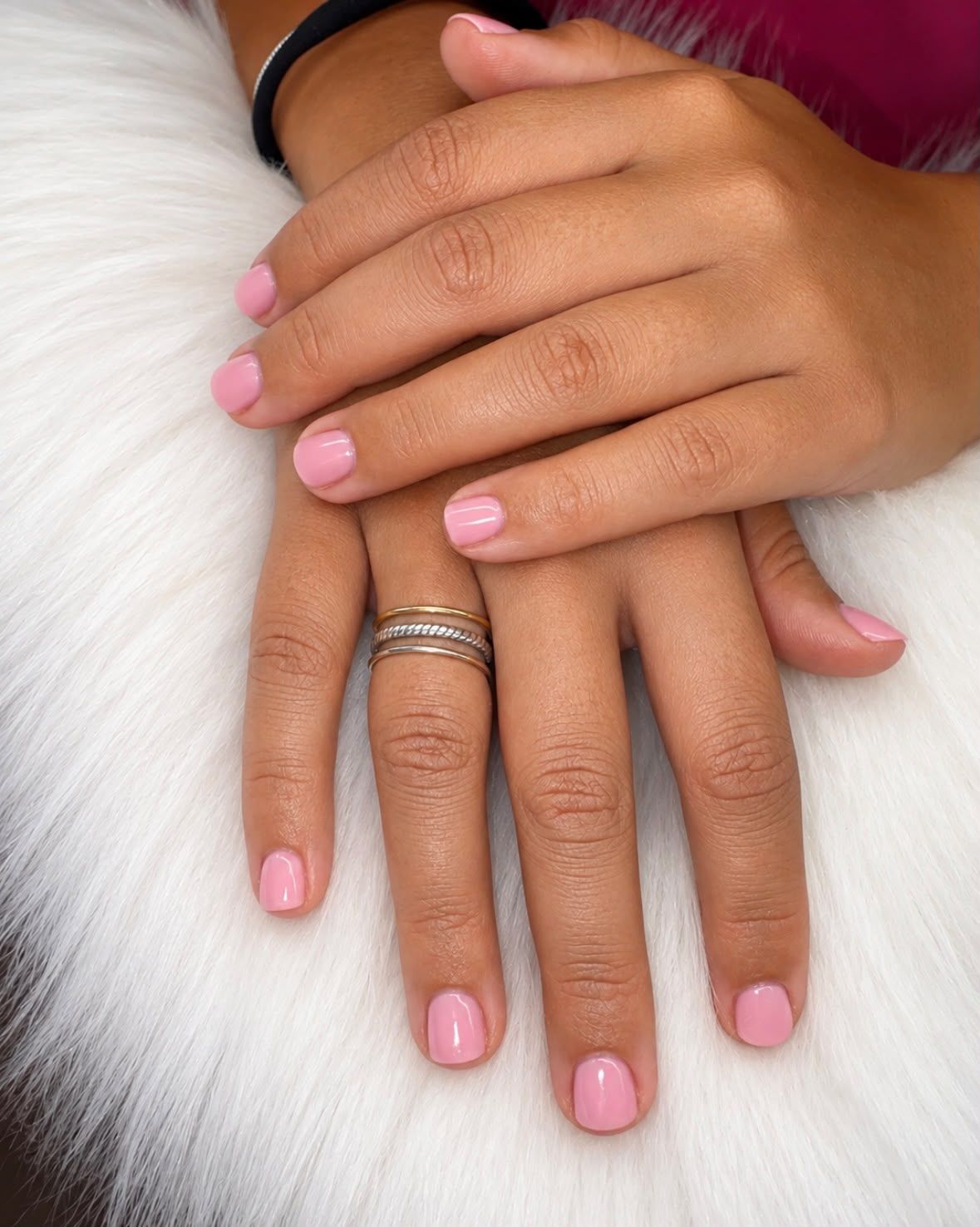 Manos con uñas de color rosa claro y un anillo de plata sobre un fondo de piel blanca.