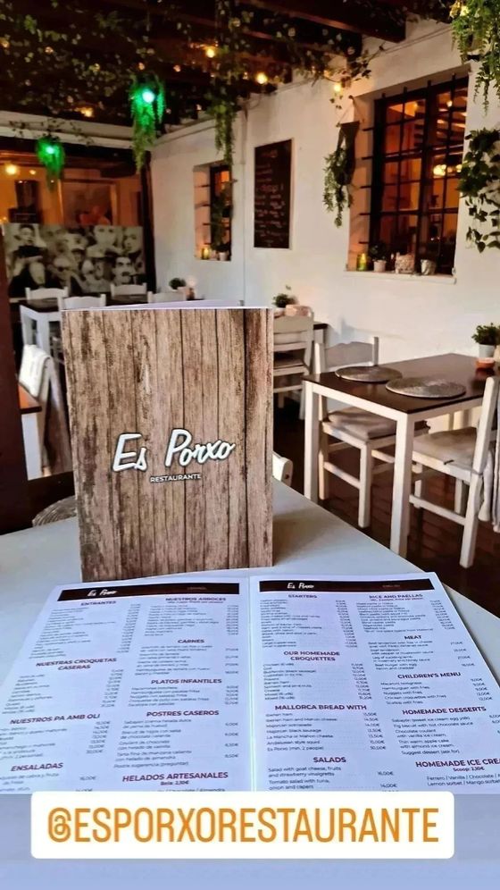 Interior de restaurante con un menú de madera sobre una mesa, sillas y mesas blancas, follaje.