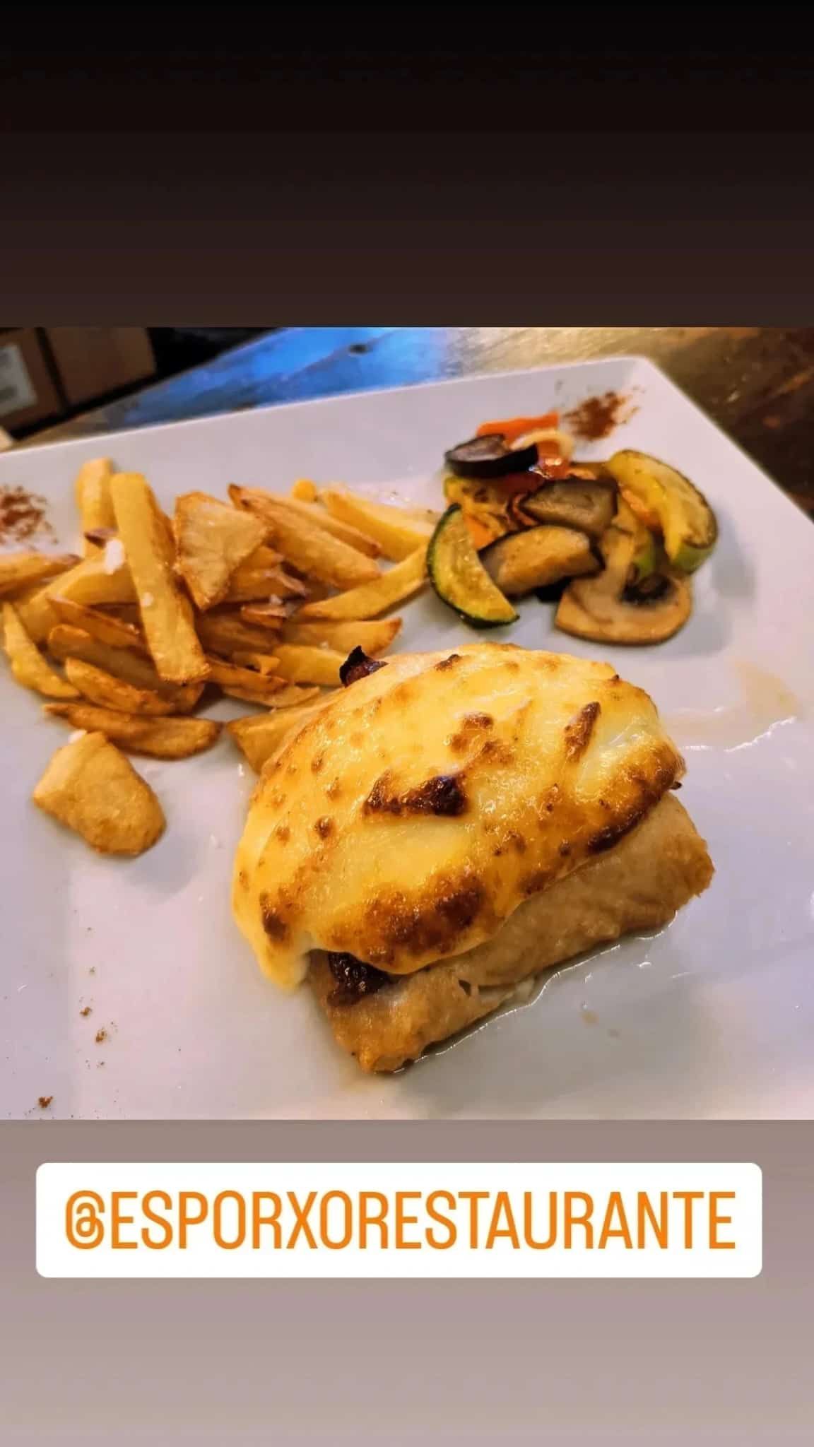 Filete de pescado con patatas fritas y verduras a la parrilla en un plato blanco en un restaurante.