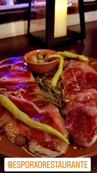 Lonchas de jamón curado sobre tostada, aceitunas, pimientos y romero en plato rústico; etiqueta