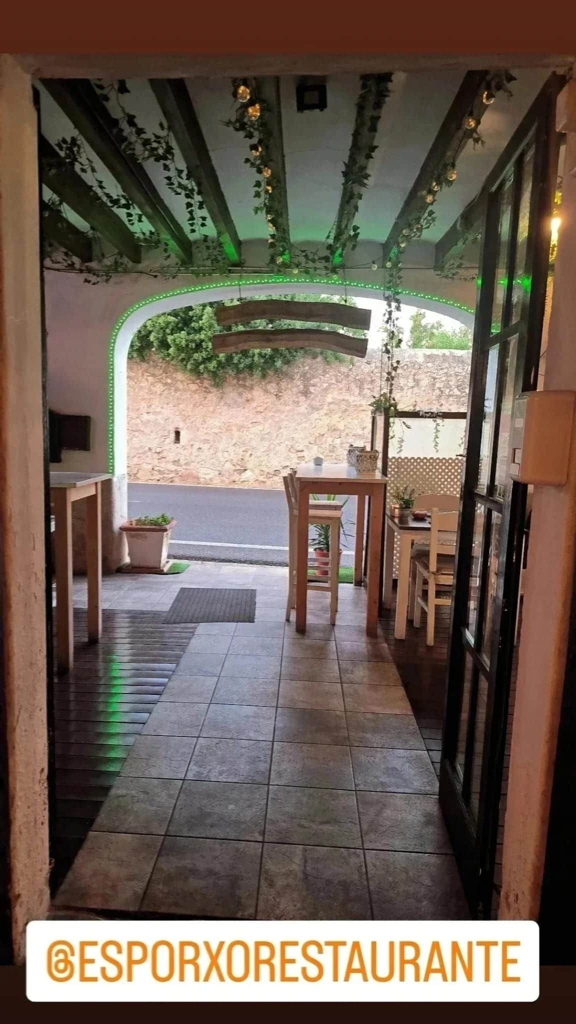 Entrada a un restaurante con mesas, decoración de techo y vista a la calle.