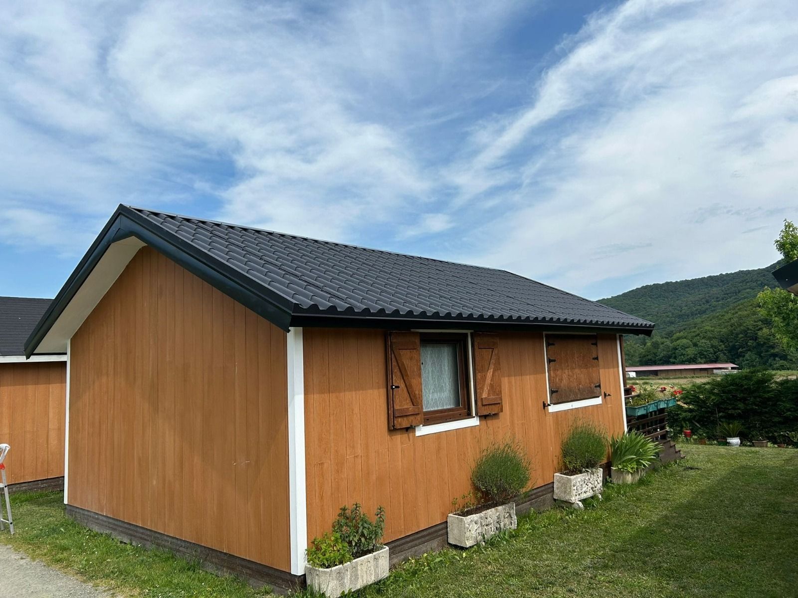 Pequeña casa naranja con techo oscuro en un paisaje rural cubierto de hierba bajo un cielo nublado.