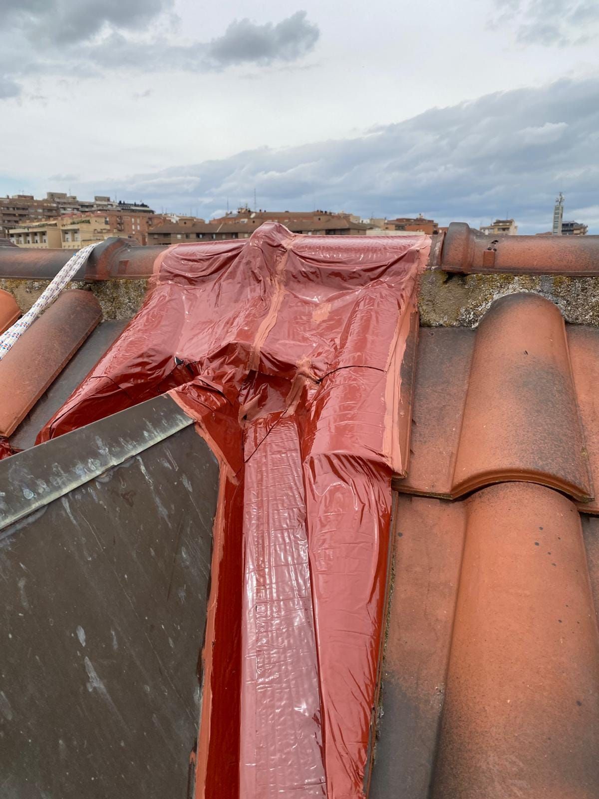 Una lona roja cubría un tejado de terracota dañado bajo un cielo nublado.