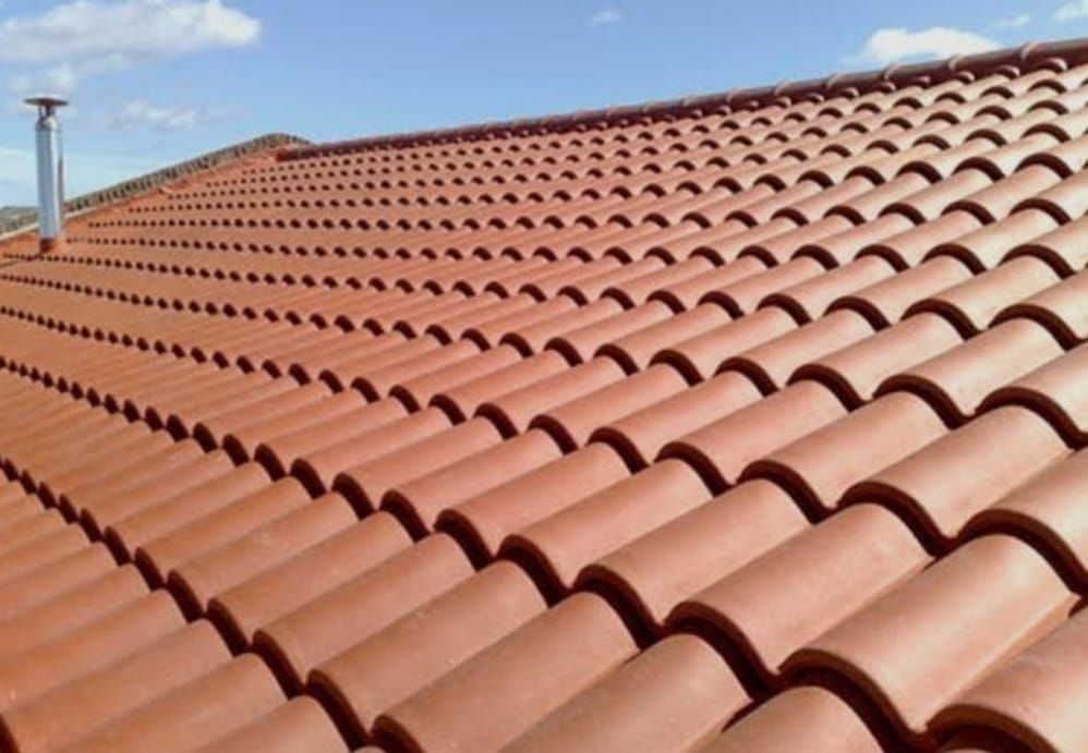 Techo de tejas de terracota roja con hileras de tejas curvas bajo un cielo azul claro.