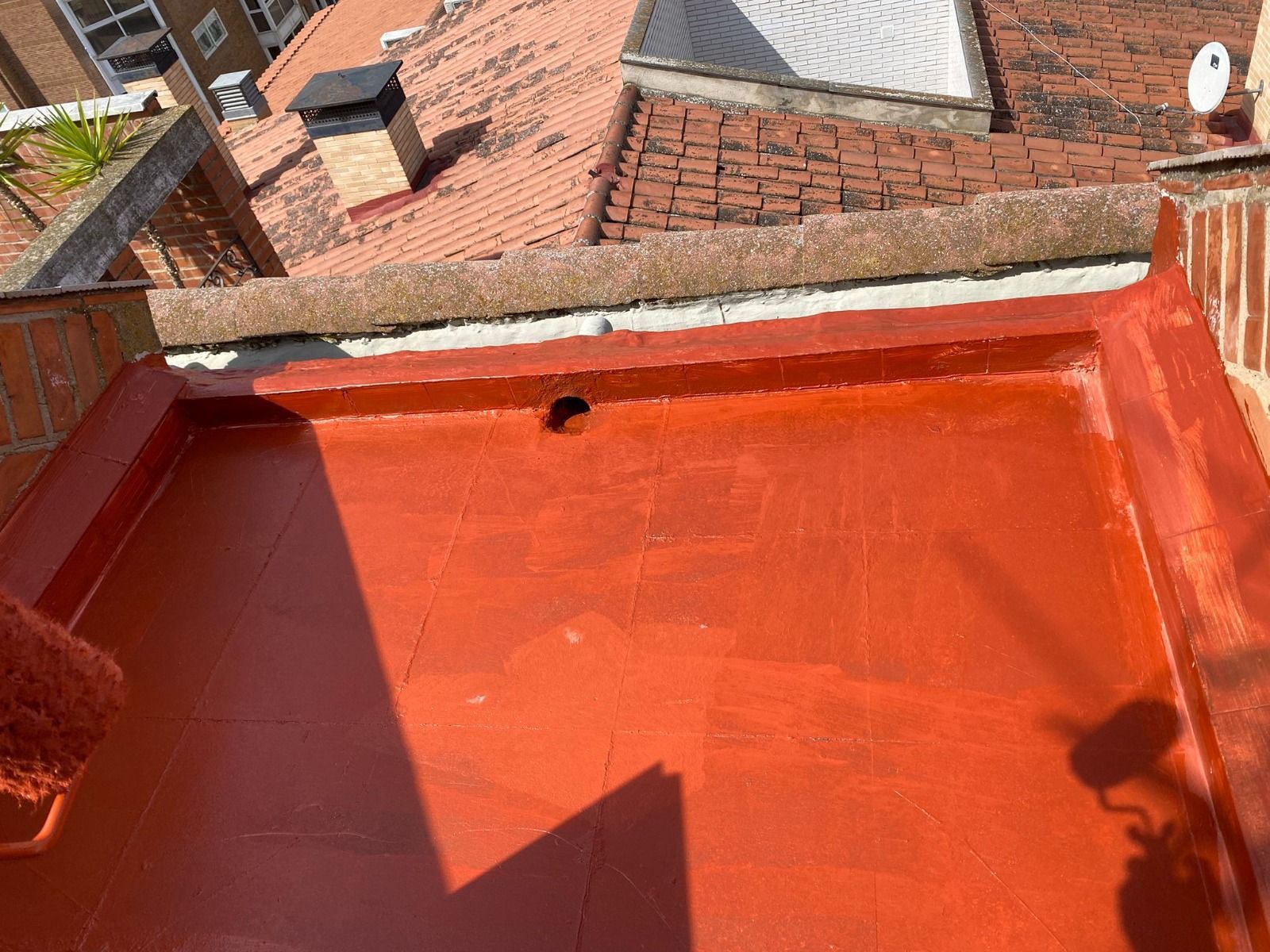 Terraza roja en la azotea con suelo naranja y muro bajo, con vistas a los tejados de tejas de los vecinos.
