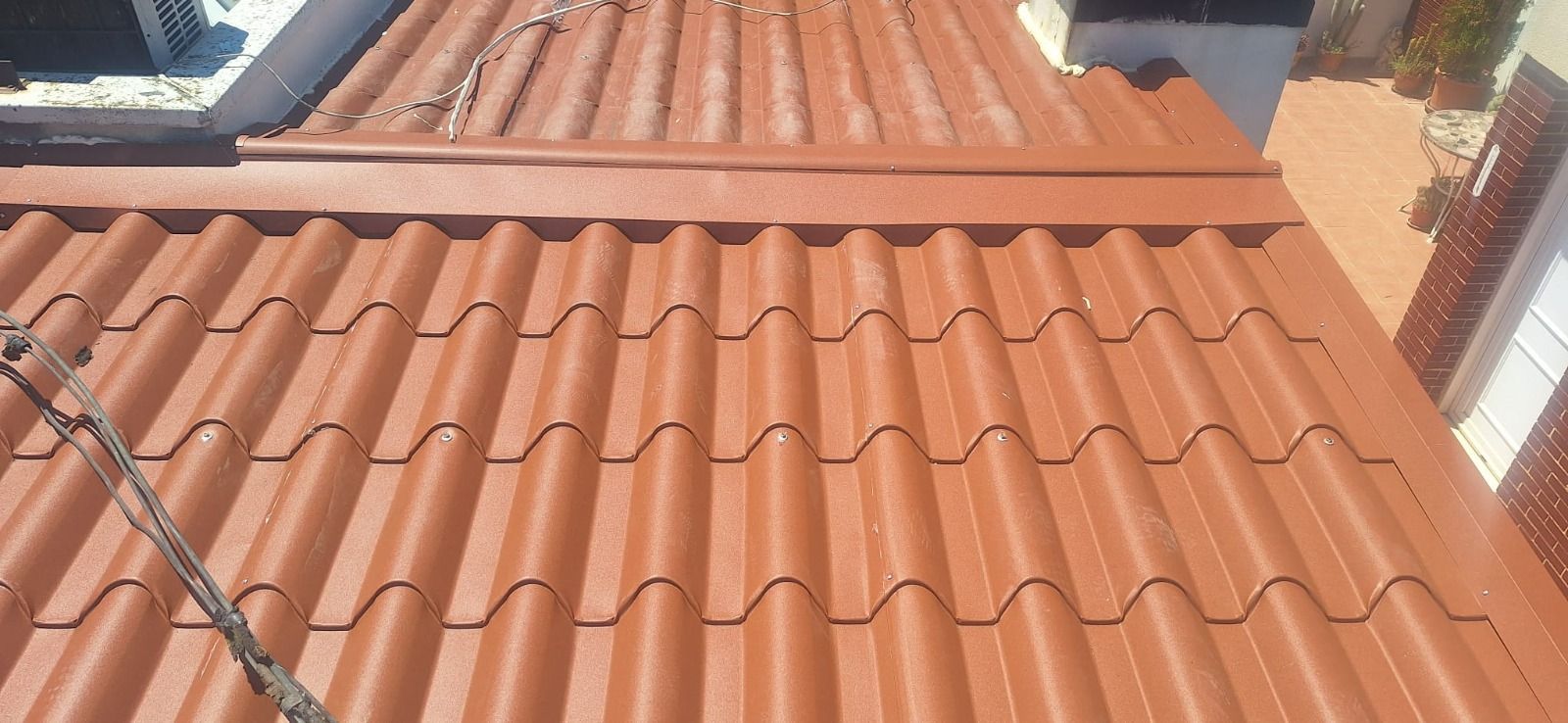 Techo de tejas de arcilla roja con tuberías en la azotea y una pequeña claraboya bajo la luz brillante del sol.