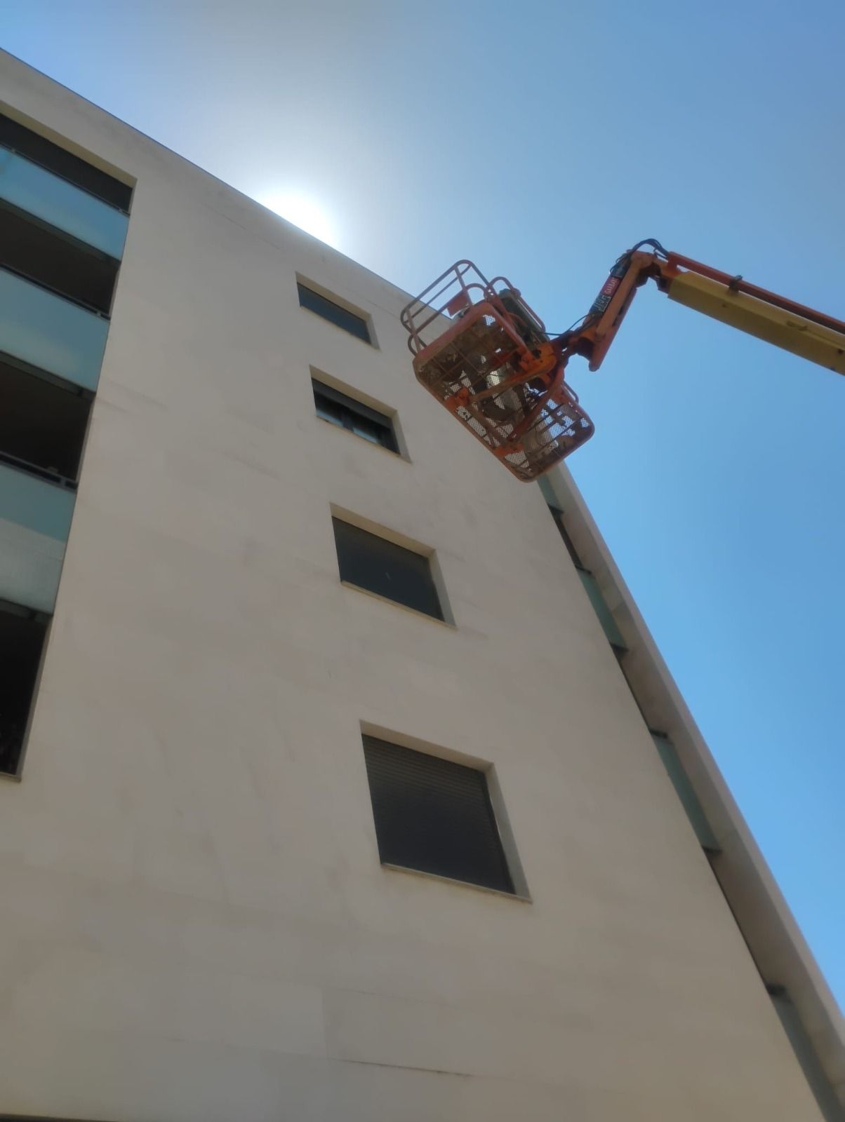 Una cesta de ascensor naranja junto a un edificio blanco alto bajo un cielo azul brillante.