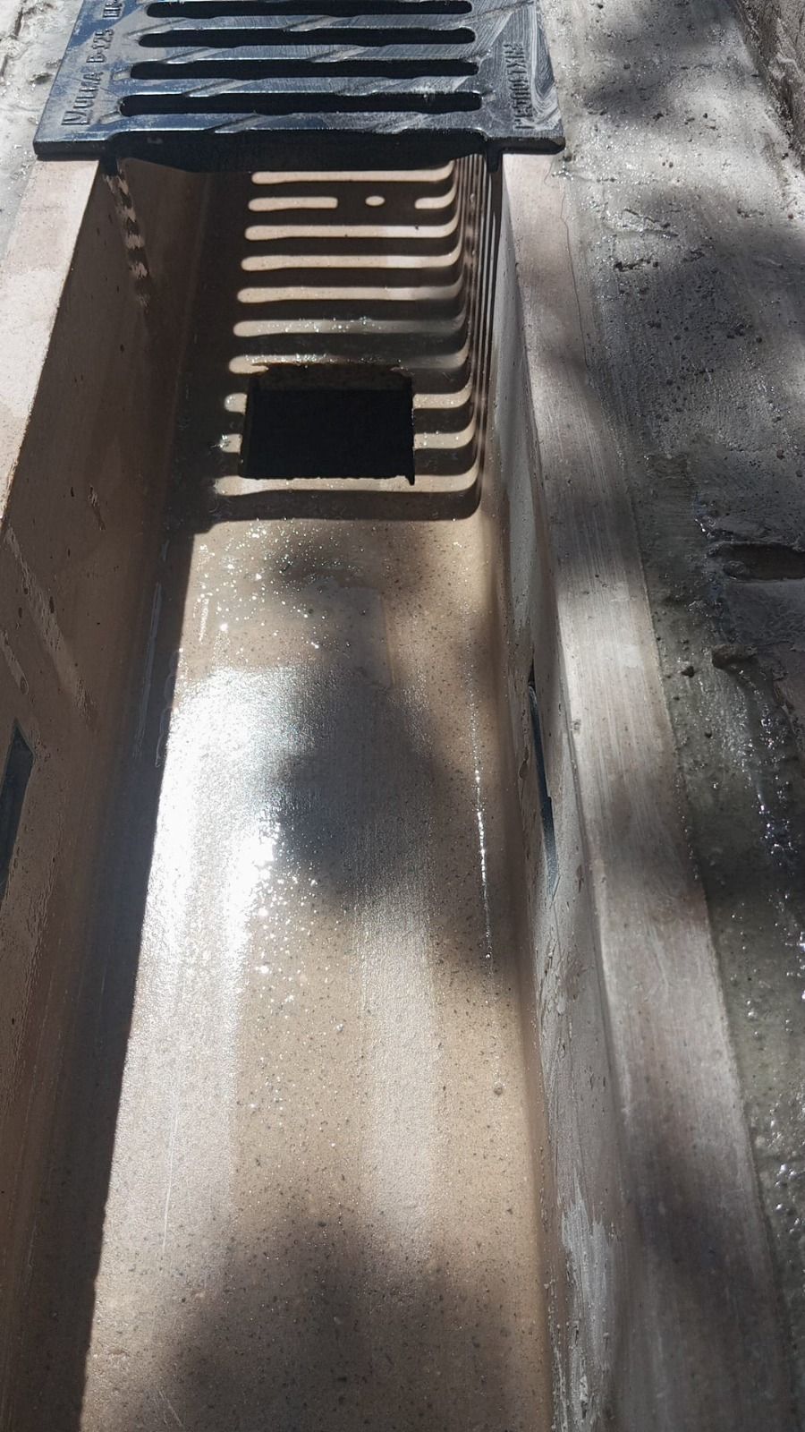 Primer plano de una alcantarilla pluvial con rejilla metálica y restos de pavimento mojado.