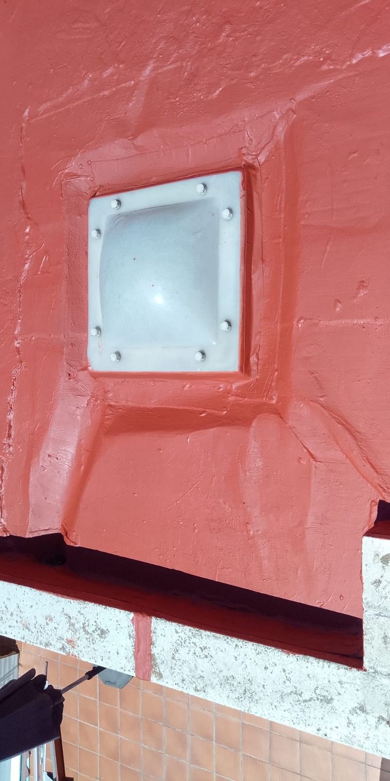 Tapa de ventilación cuadrada blanca sobre una pared roja encima de una repisa de azulejos.