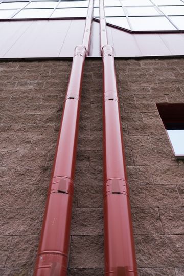 Dos bajantes rojos recorren la pared rugosa de un edificio, debajo de una hilera de ventanas.