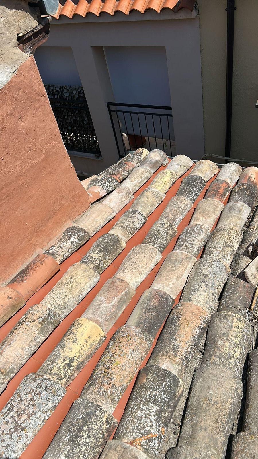 Vista desde la azotea de tejas de arcilla roja desgastadas que dan a un edificio gris y un callejón.