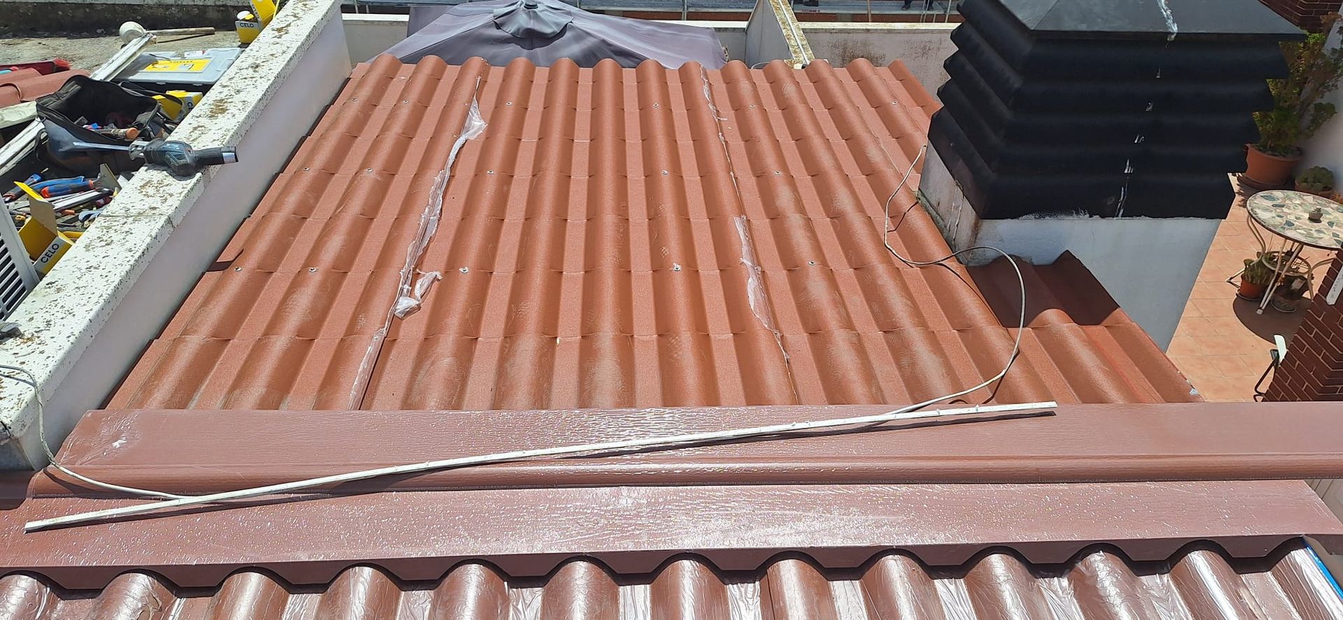 Azotea con paneles de metal corrugado color óxido y rejillas de ventilación negras junto a tejas de terracota.