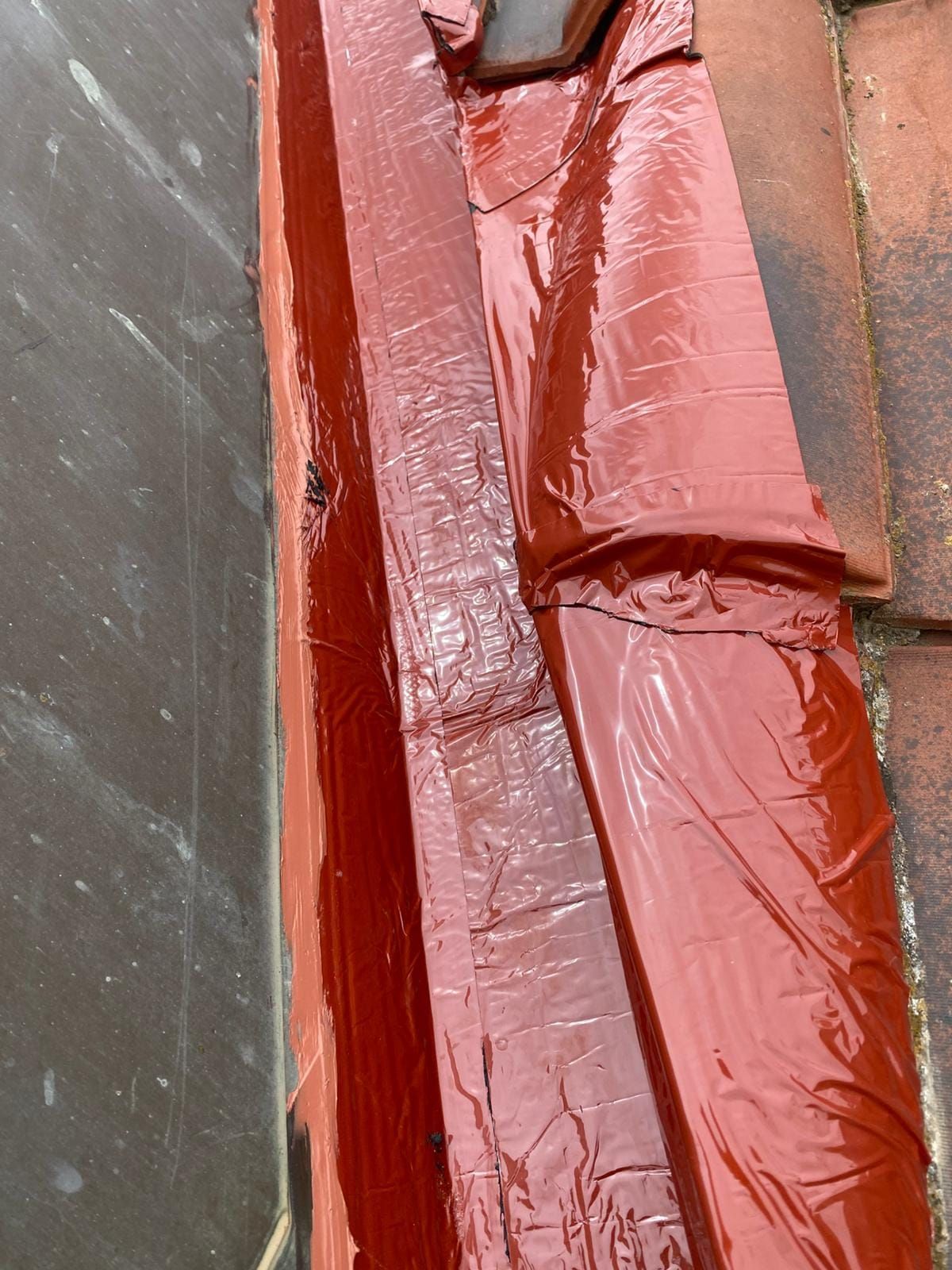 Lona o tela roja arrugada colocada entre una pared gris y una superficie de color marrón rojizo.