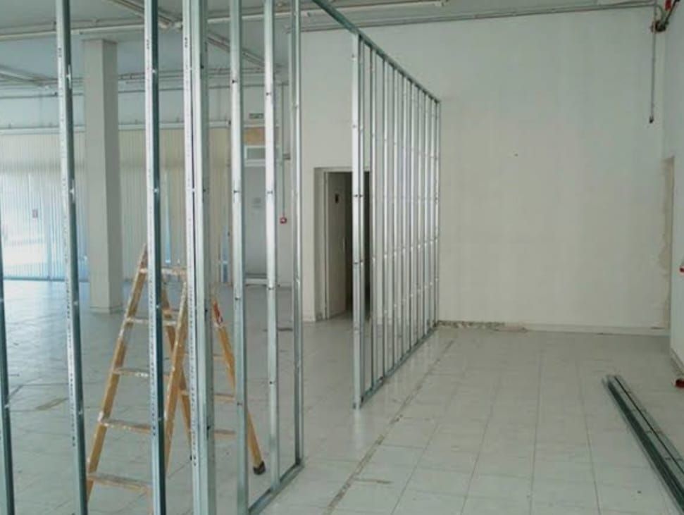 Interior vacío con estructura metálica en las paredes, una escalera y suelo de baldosas en construcción.