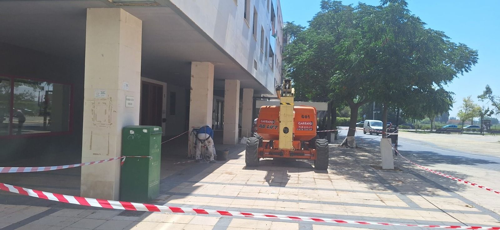 Vehículo de mantenimiento rojo junto a la entrada de un edificio, con cinta de seguridad roja