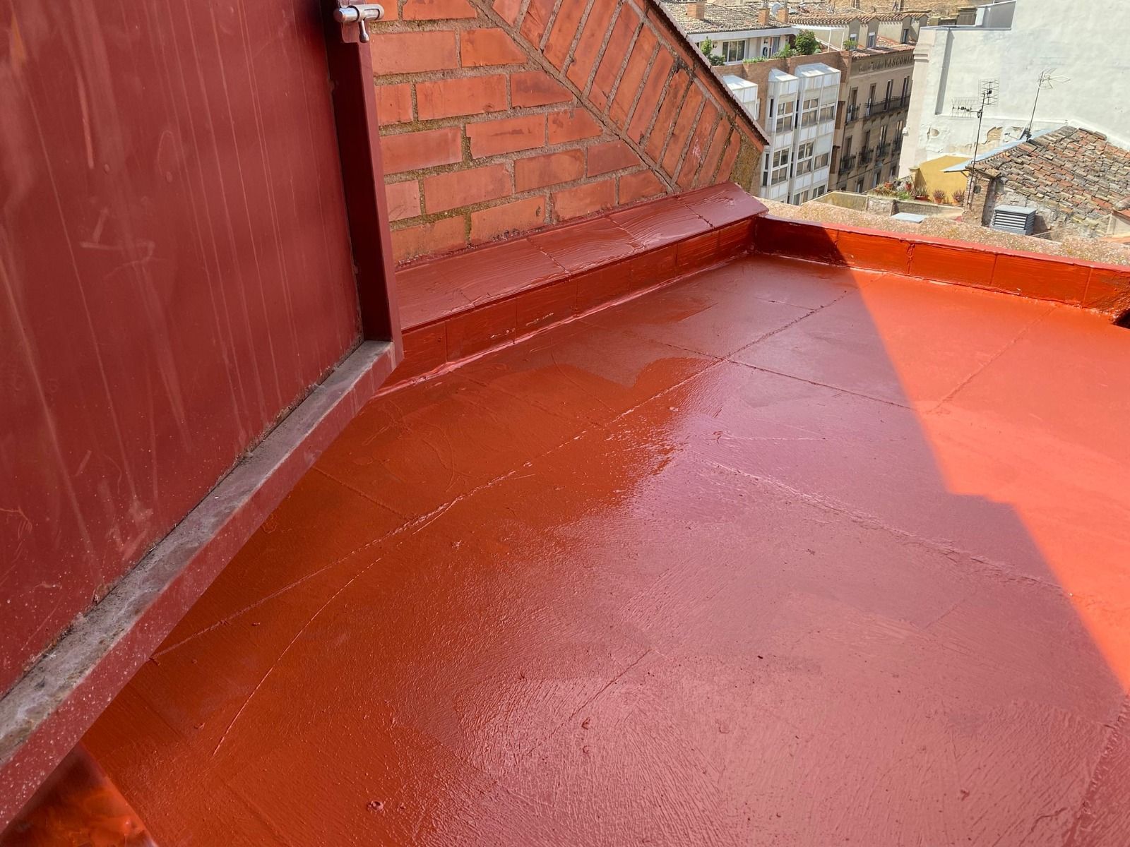 Terraza en la azotea pintada de rojo con pared de ladrillo y edificios de la ciudad al fondo.