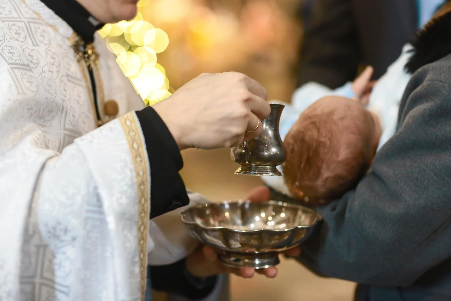 Sacerdote vertiendo agua sobre la cabeza de un bebé durante una ceremonia de bautismo.
