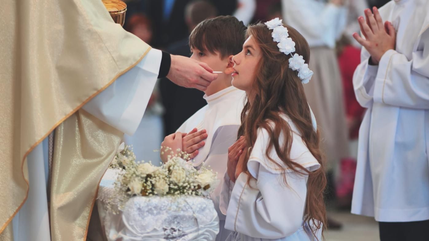 Una jovencita se arrodilla en oración durante una ceremonia religiosa junto a un ramo de flores 