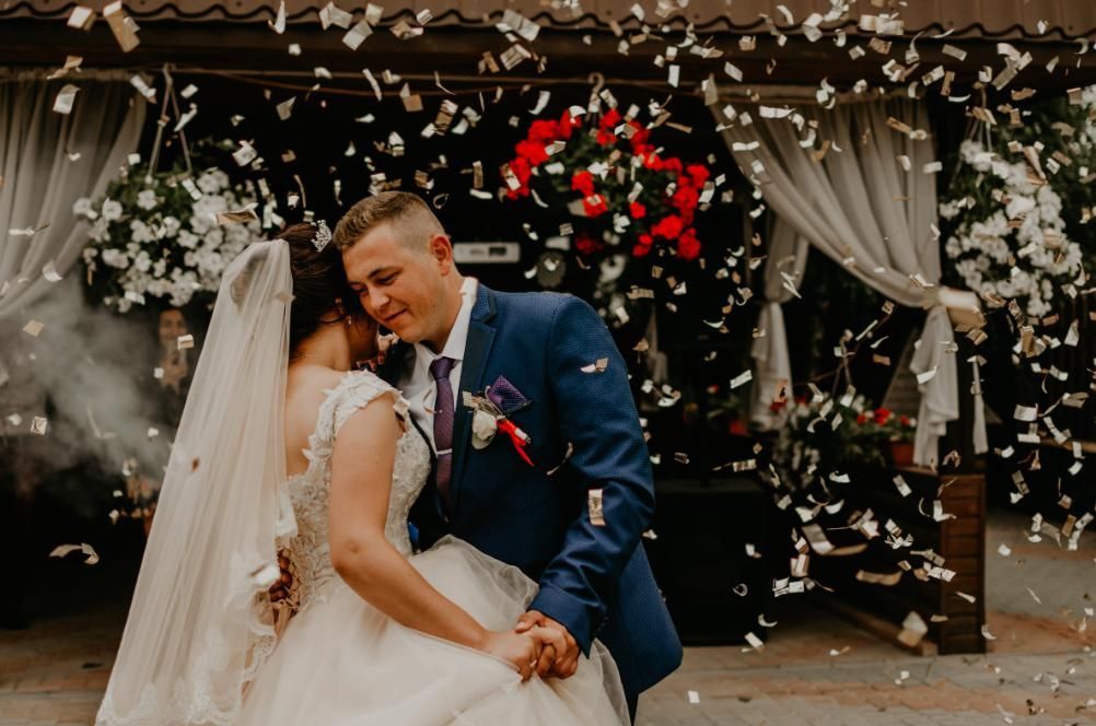 Pareja de recién casados ​​besándose bajo pétalos que caen bajo un arco floral