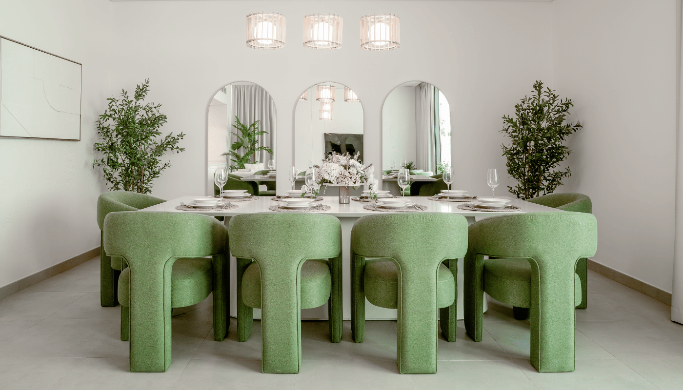 Elegant dining room with pastel green upholstered chairs, white table setting, mirrors, and potted trees