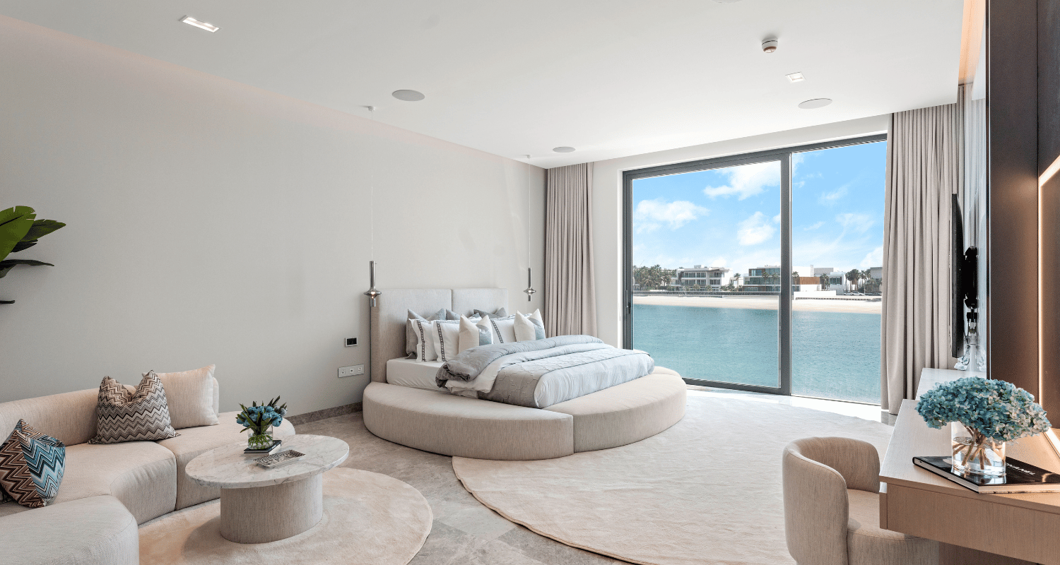 Bright modern bedroom with a round bed, neutral decor, and large windows overlooking the water