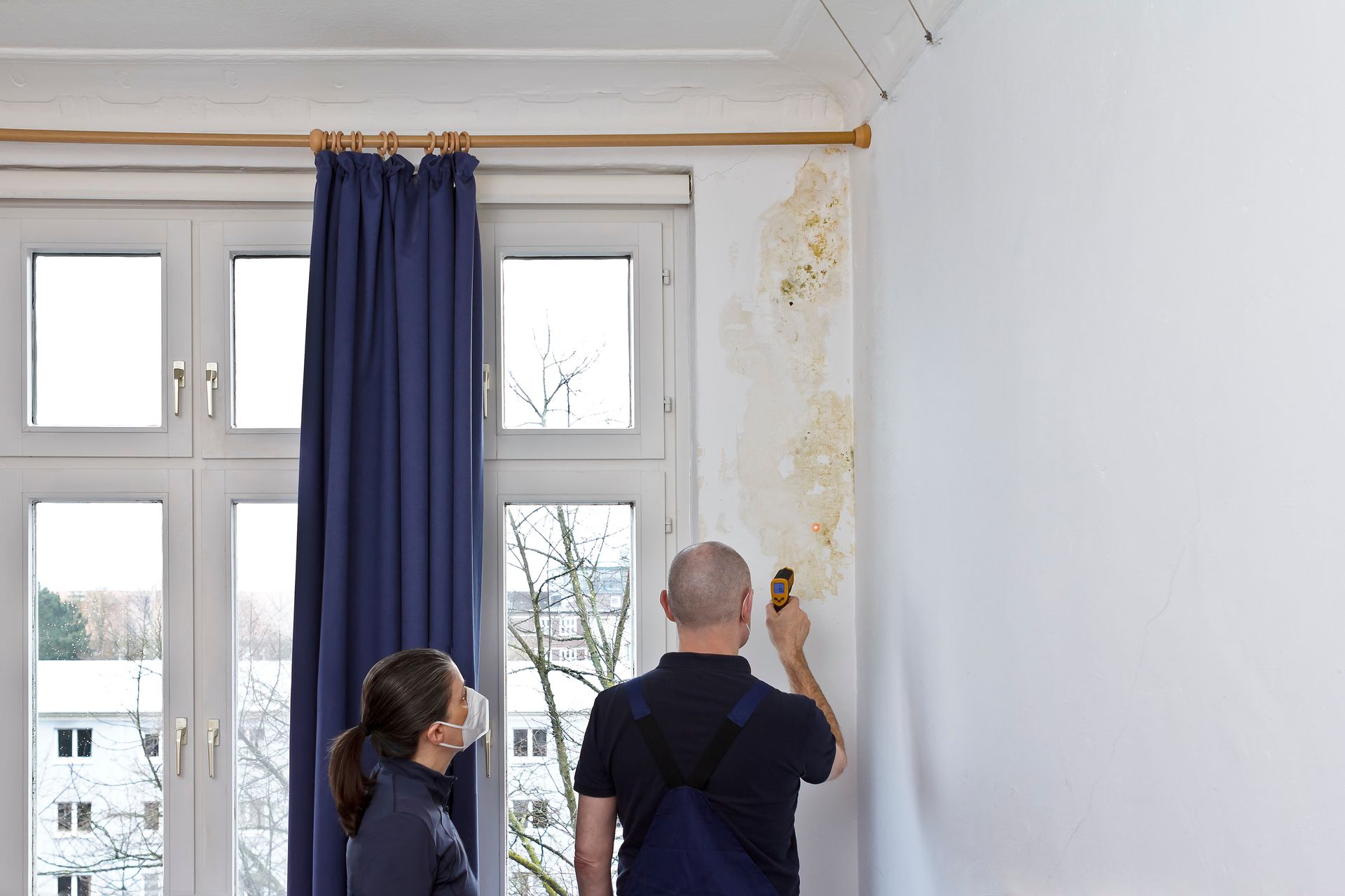 Fachpersonal misst Feuchtigkeit an schimmelbefallener Wand – Vorbereitung zur Schimmelsanierung in Wohnraum