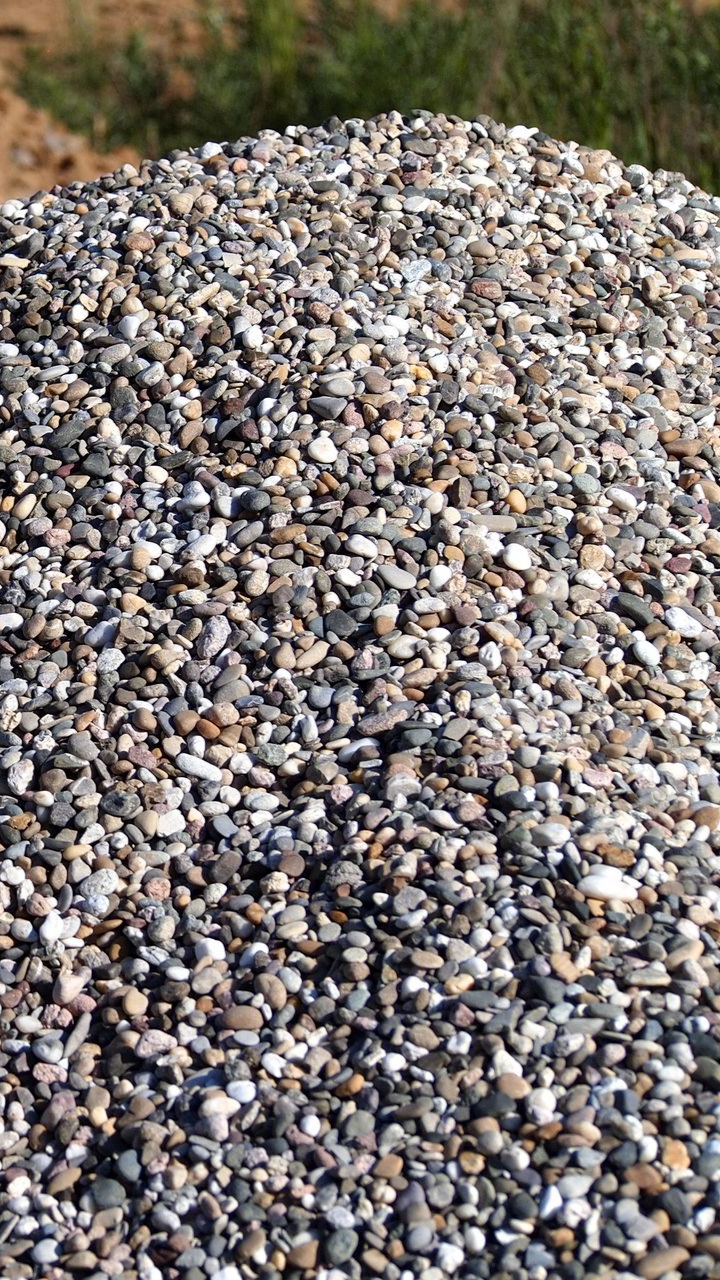 Tas de petits cailloux de couleurs mélangées, destinés à l'aménagement paysager, avec de l'herbe verte en arrière-plan.