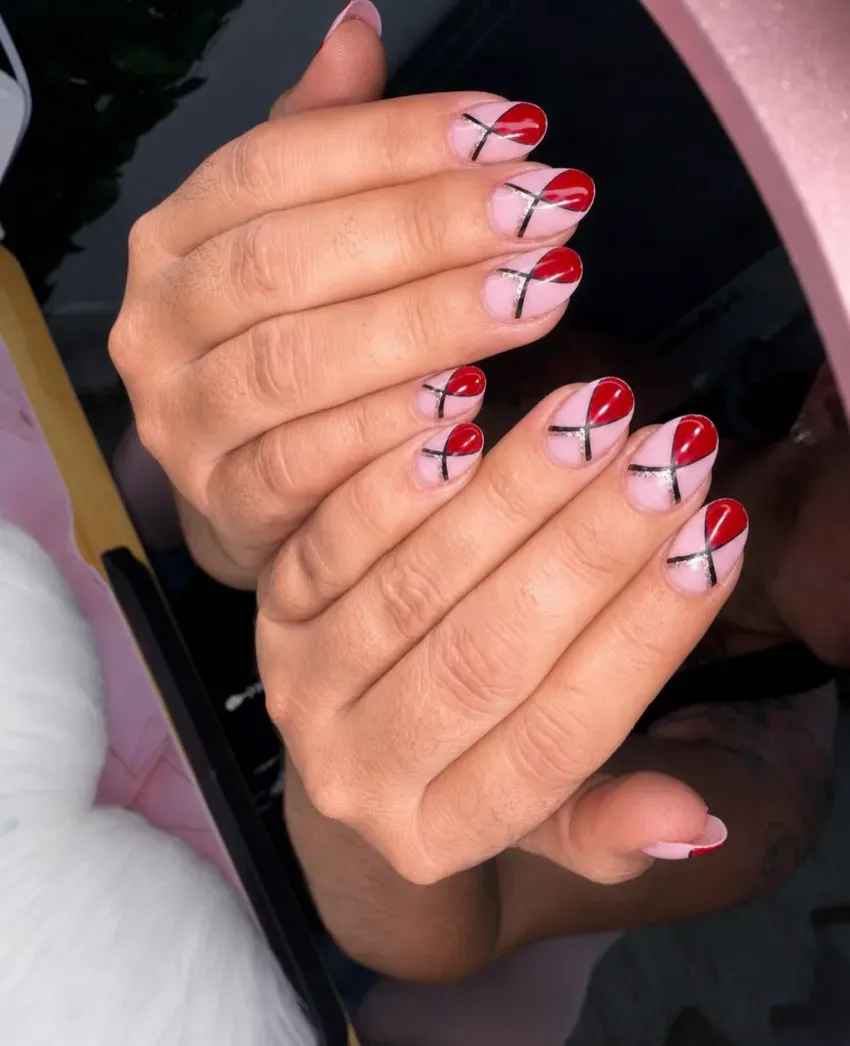 Manos con uñas decoradas con diseños abstractos en rojo, blanco y negro sosteniendo un teléfono.