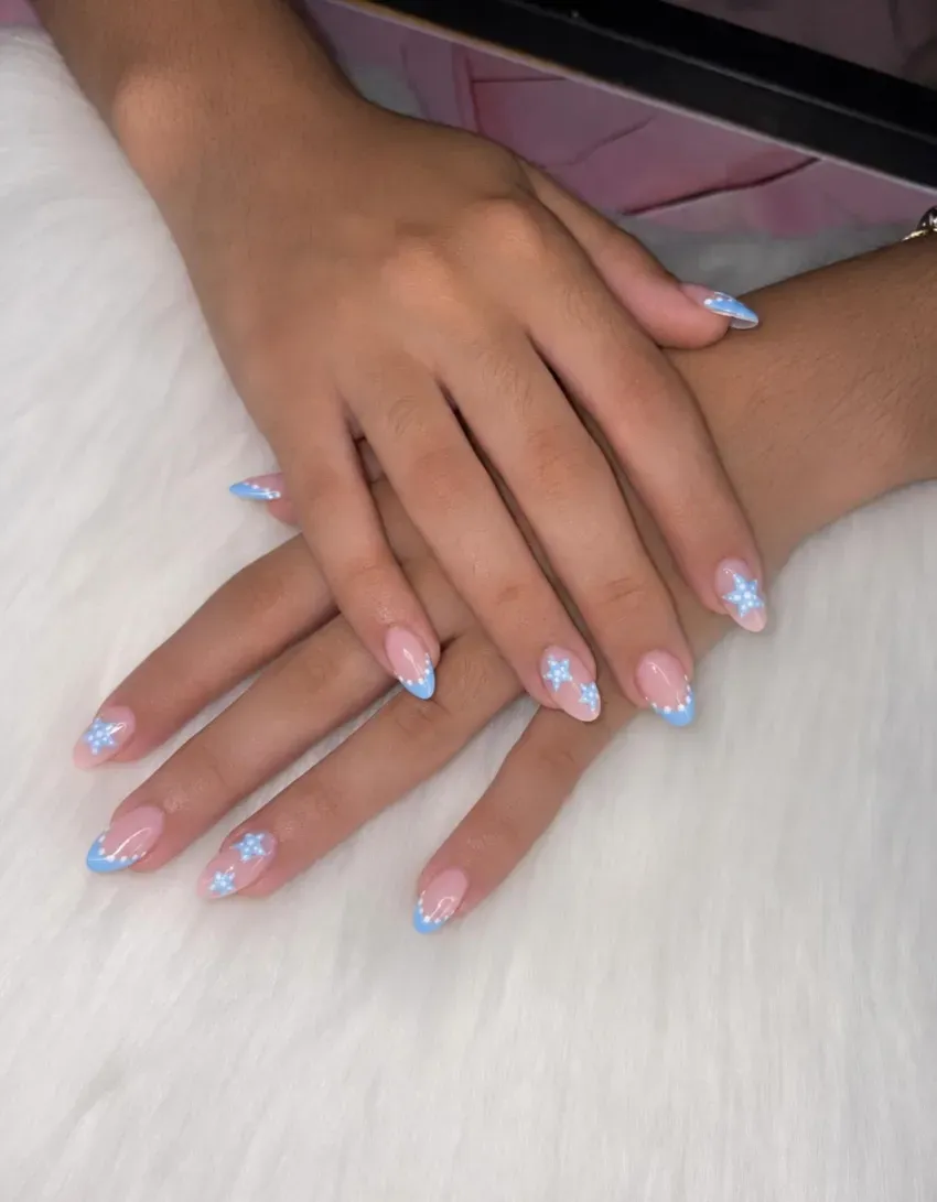 Manos con uñas de purpurina azul claro descansando sobre una superficie de piel blanca.
