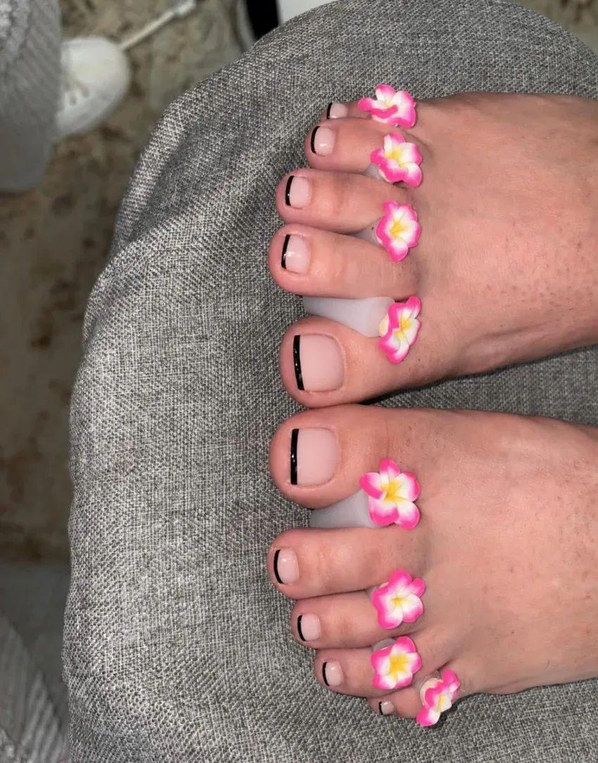 Primer plano de dos pies con anillos de flores rosas y blancas en los dedos sobre tela gris.
