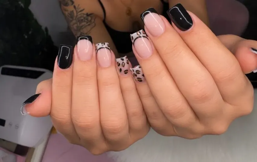 Manos con uñas bien cuidadas, con esmalte negro brillante y rosa pálido con detalles florales blancos.