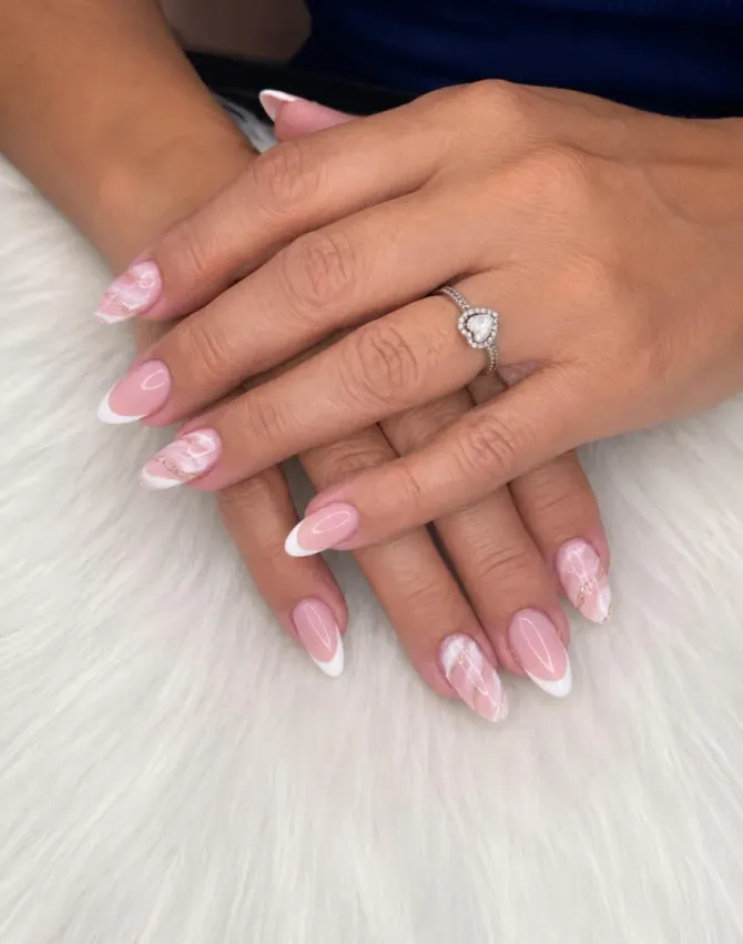 Manos con manicura francesa rosa y anillo de diamantes descansando sobre una superficie de piel blanca.
