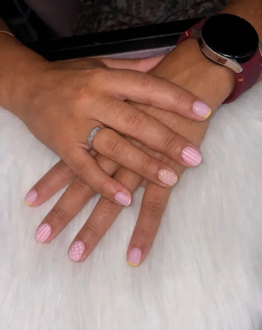 Dos manos con uñas rosas y anillos descansando sobre una superficie de piel blanca; una de ellas lleva un reloj.