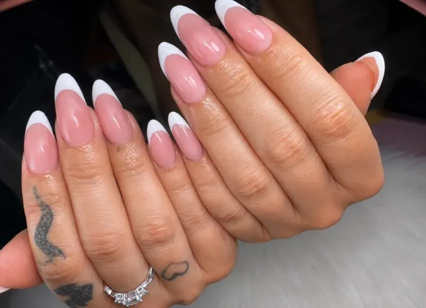 Manos con uñas acrílicas largas de color rosa y blanco con punta francesa y anillos de plata, mostradas en primer plano.